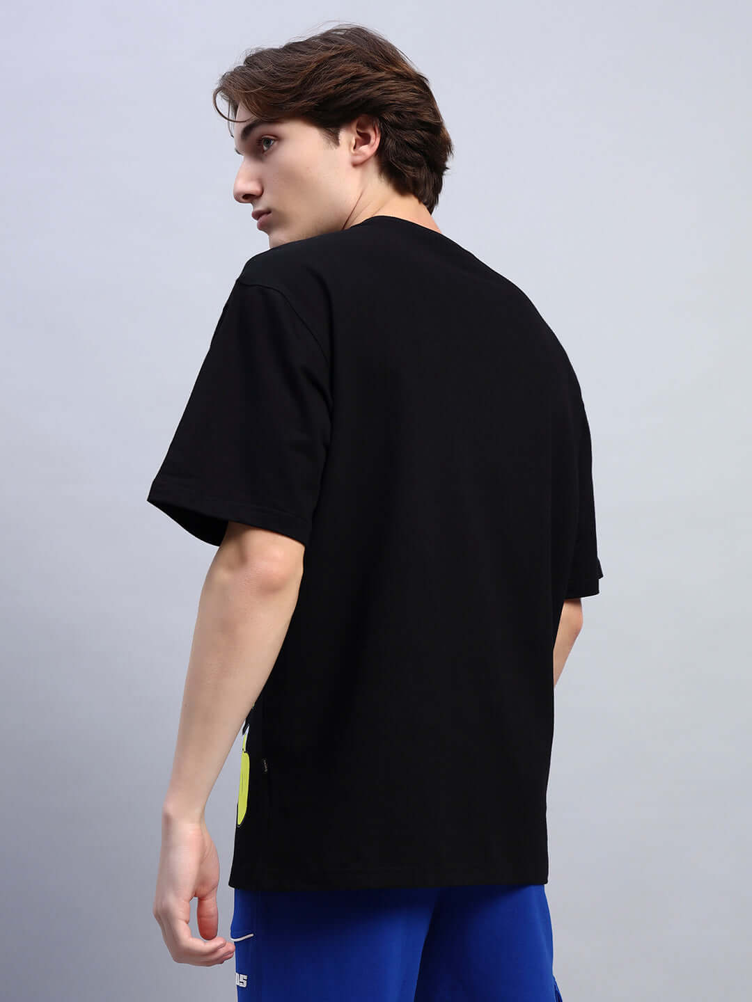 Rear view of model in a DONALD DUCK PRINTED OVERSIZED T-SHIRT BLACK and blue shorts, showcasing relaxed silhouette and casual style.
