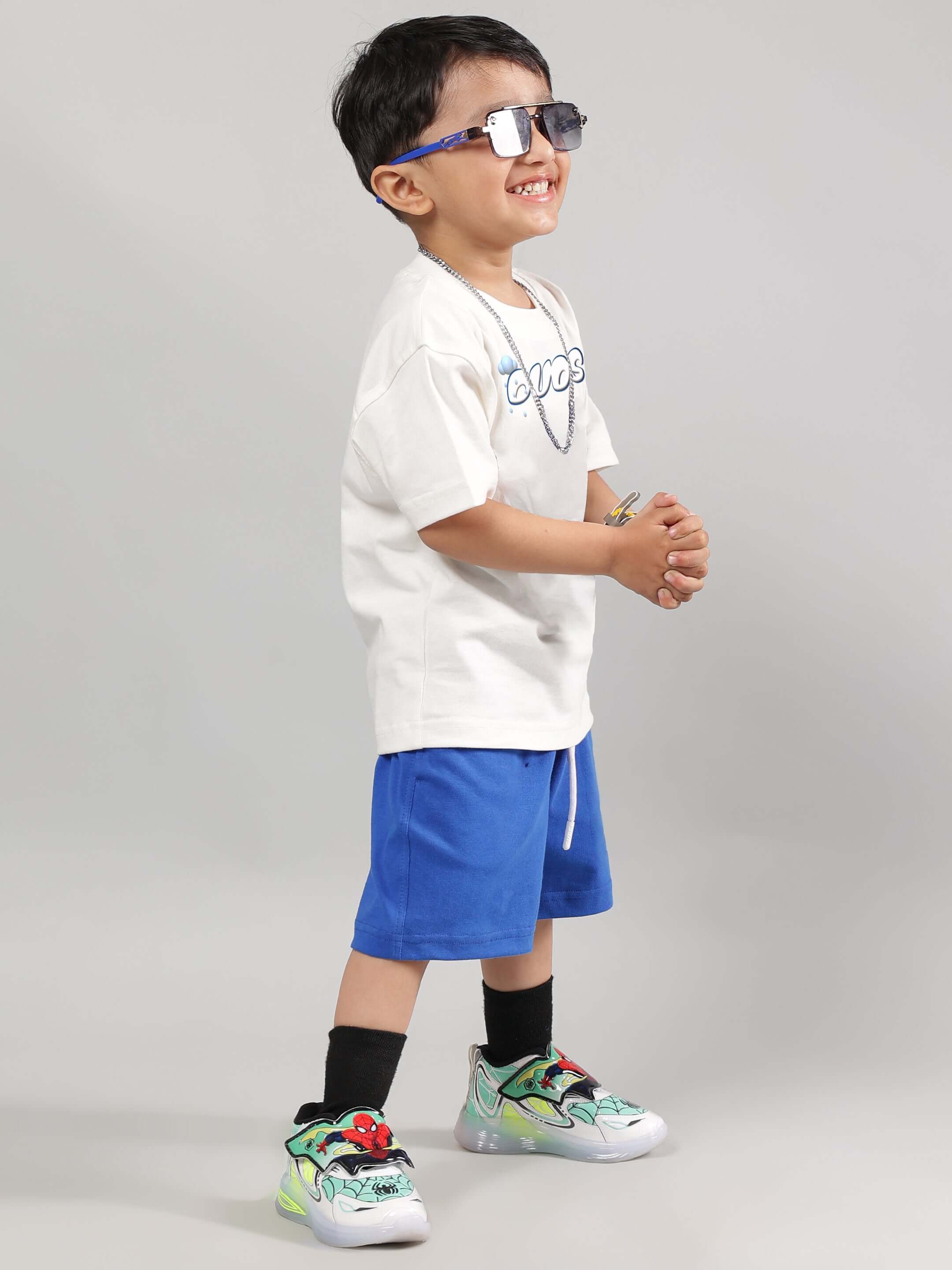Child wearing Doraemon-themed summer co-ord set in off-white and royal blue, featuring trendy sneakers and sunglasses.