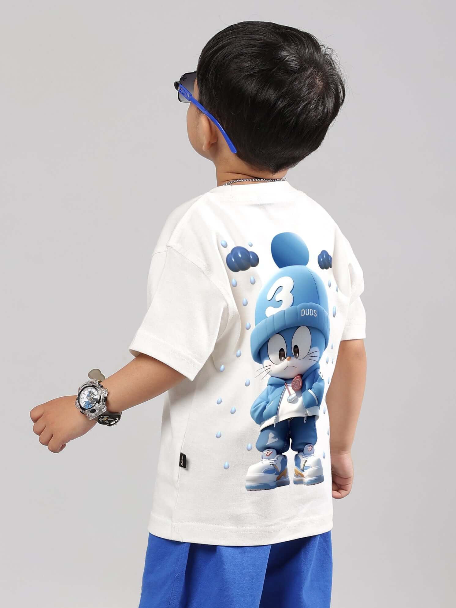 Child wearing off-white Doraemon t-shirt featuring cartoon character on back, perfect for boys and girls, crafted by DUDS tailors.
