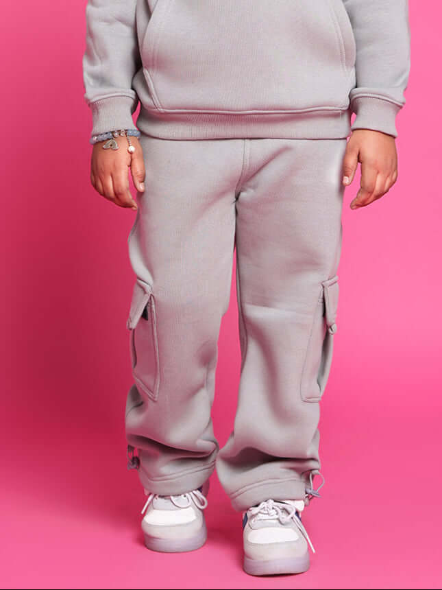 Child wearing Dream Fleece Pant for Boys and Girls in grey, standing against a pink background, showing comfort and casual style.