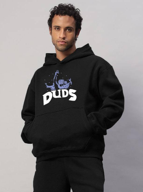 Man wearing WEARDUDS DREAMER FLEECE HOODIE BLACK with logo, standing in front of light grey background.