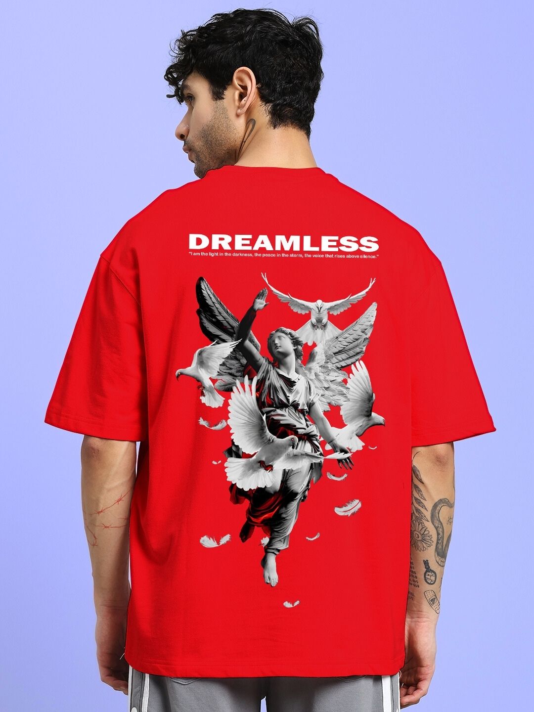 Alt Tag: Man wearing DREAMLESS OVER-SIZED T-SHIRT RED with angel graphic, back view, against blue background.