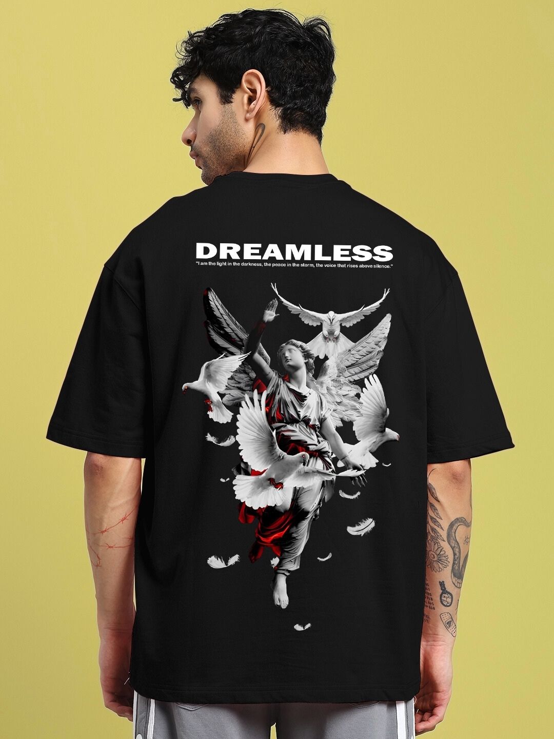 Man wearing DREAMLESS OVER-SIZED T-SHIRT BLACK with artistic back design, showcasing dreamlike theme and bold style.