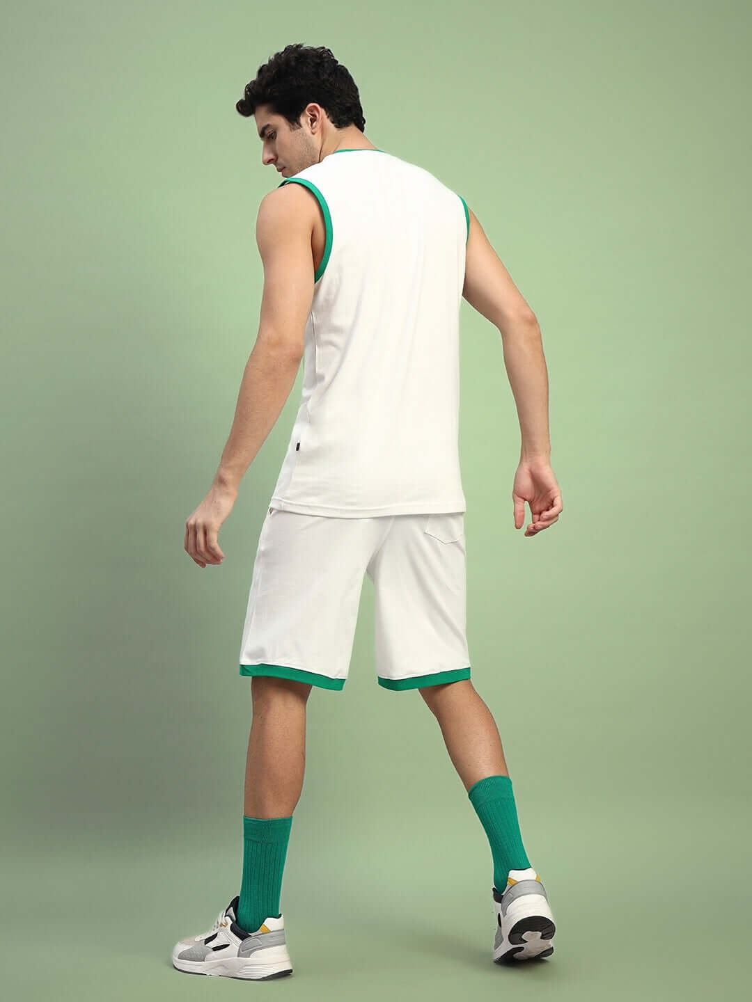 Model wearing DRIBBLE CO-ORD SET SLEEVELESS OFF WHITE in an outfit styled with athletic shoes and green socks, showing back view.