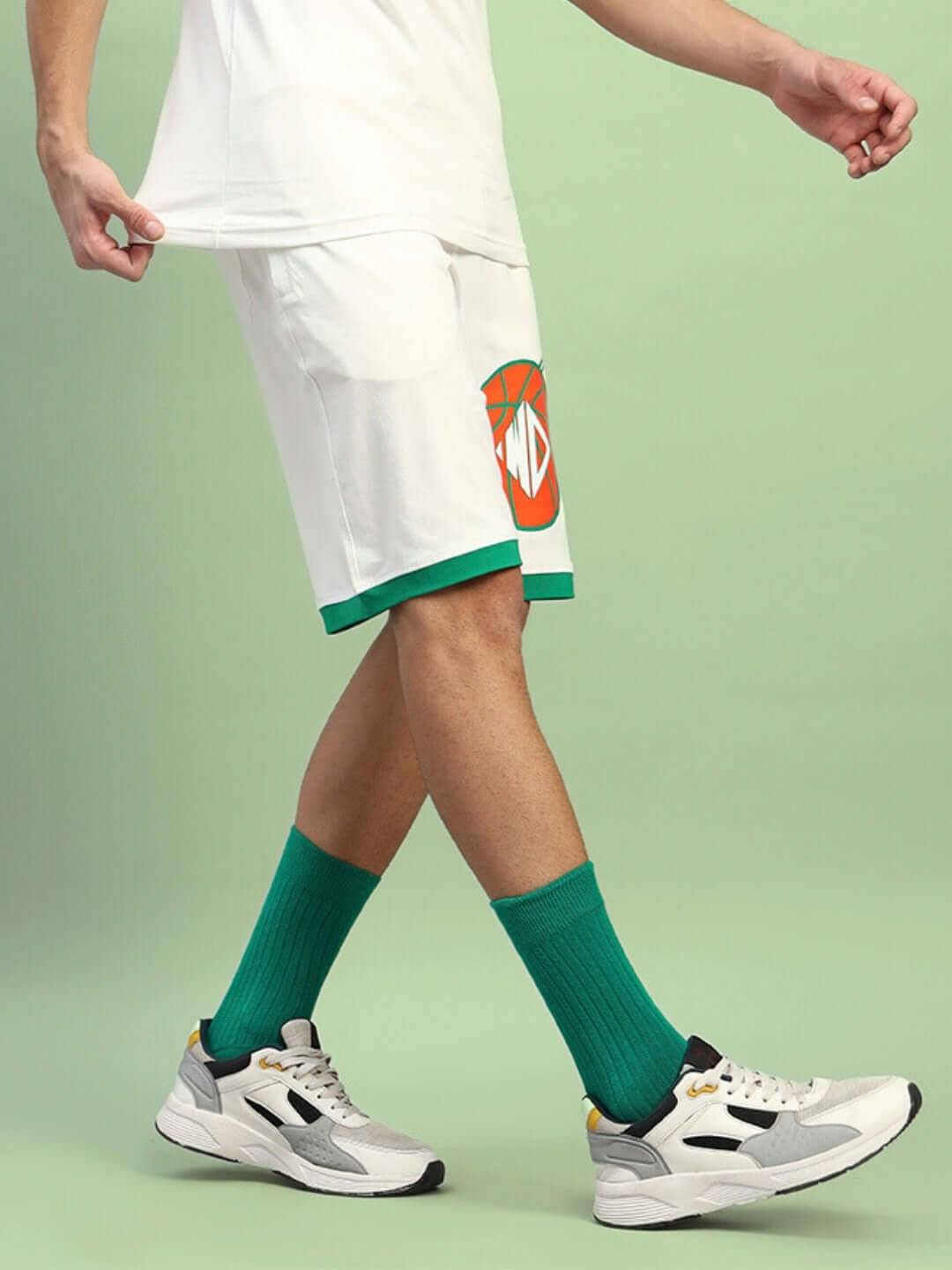 Person wearing DRIBBLE SUMMER SHORTS OFF-WHITE with green socks and sneakers against a light green background.