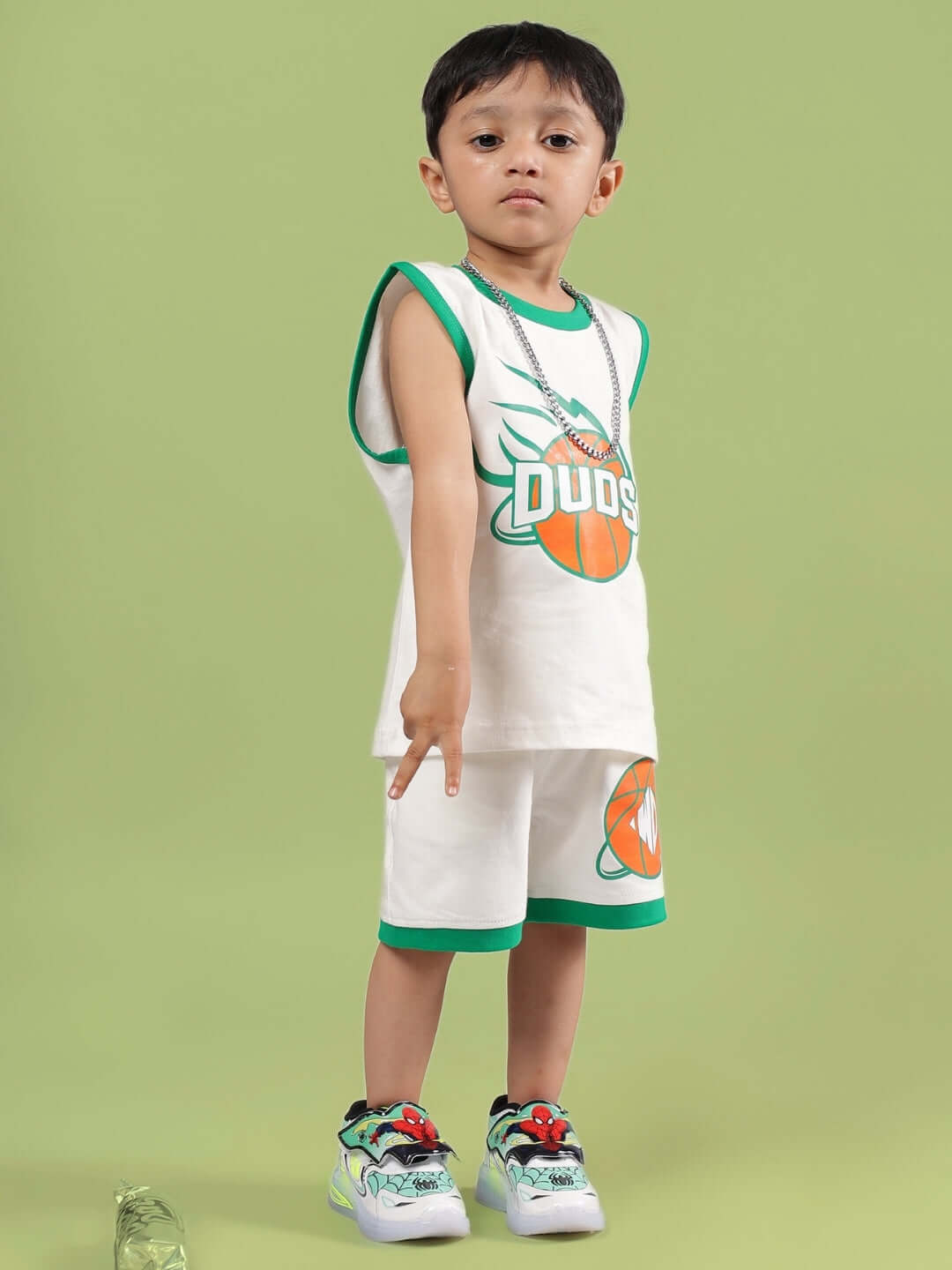 Child wearing off-white Dribble Co-ord by DUDS, sleeveless, with green trim and logo, standing against green background.