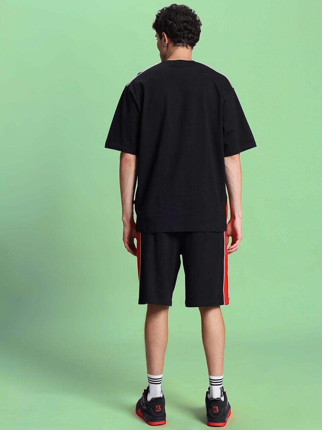 Back view of person wearing DRIFT SUMMER COTTON TERRY CO-ORD SET BLACK, showcasing relaxed-fit t-shirt and shorts on green background.
