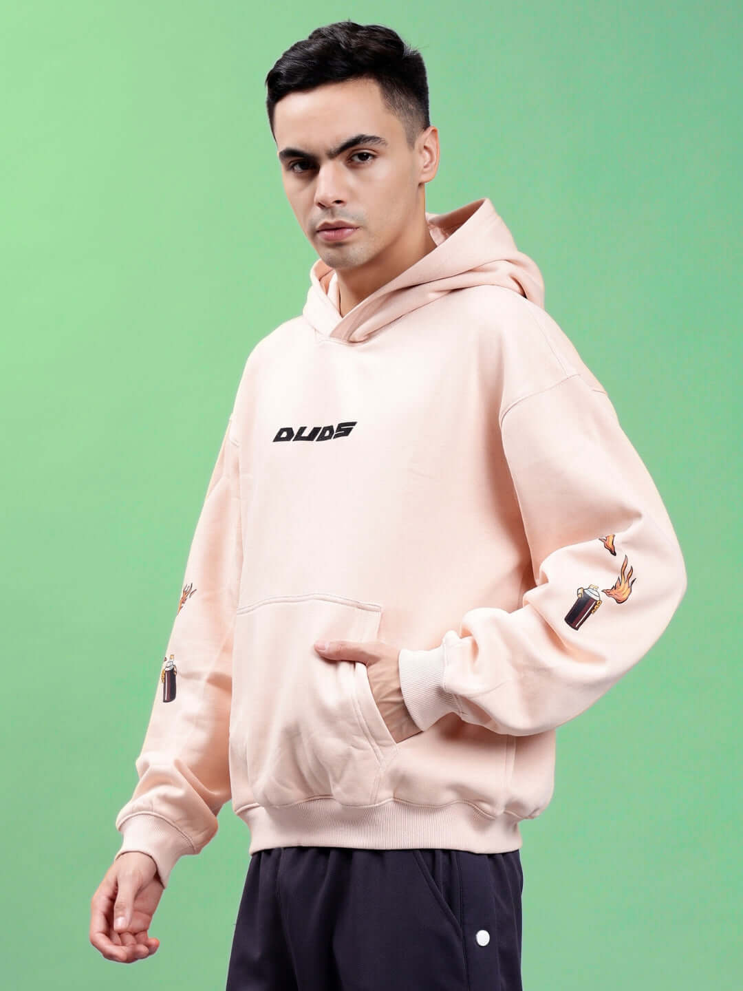 Model wearing DRIP CUPID OVERSIZED HOODIES BEIGE, showcasing streetwear style with bold graphics on the sleeves.