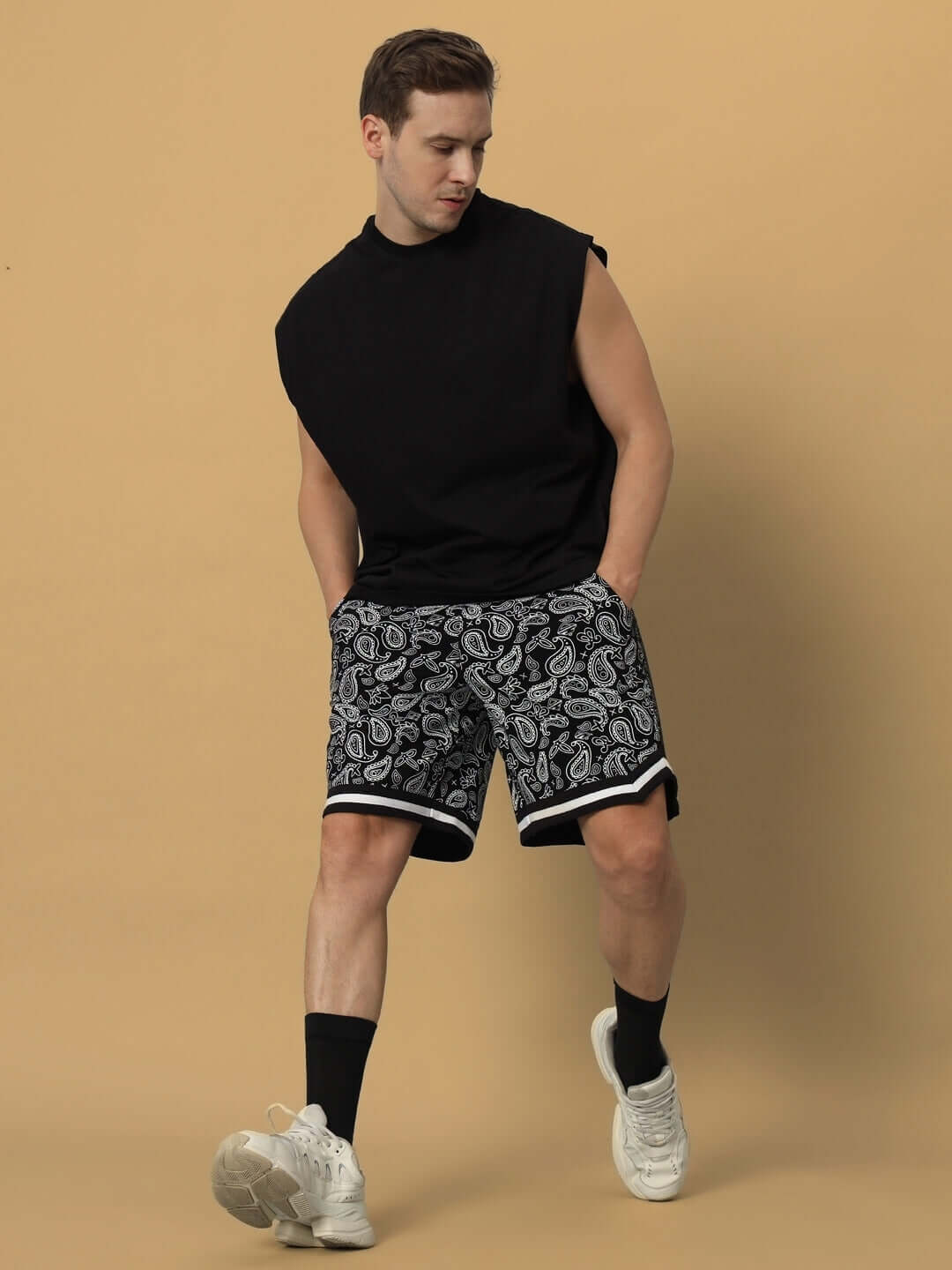 Man wearing black DRIZZLE regular fit shorts featuring a paisley design, paired with a sleeveless black top and sneakers.