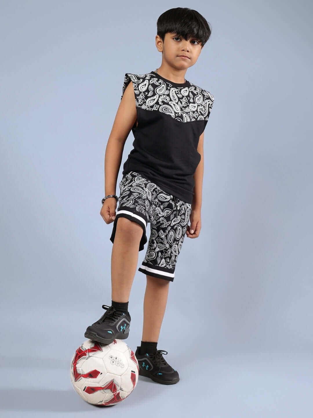 Child wearing DRIZZLE SHORTS FOR BOYS & GIRLS BLACK with intricate patterns, posing confidently with a soccer ball.