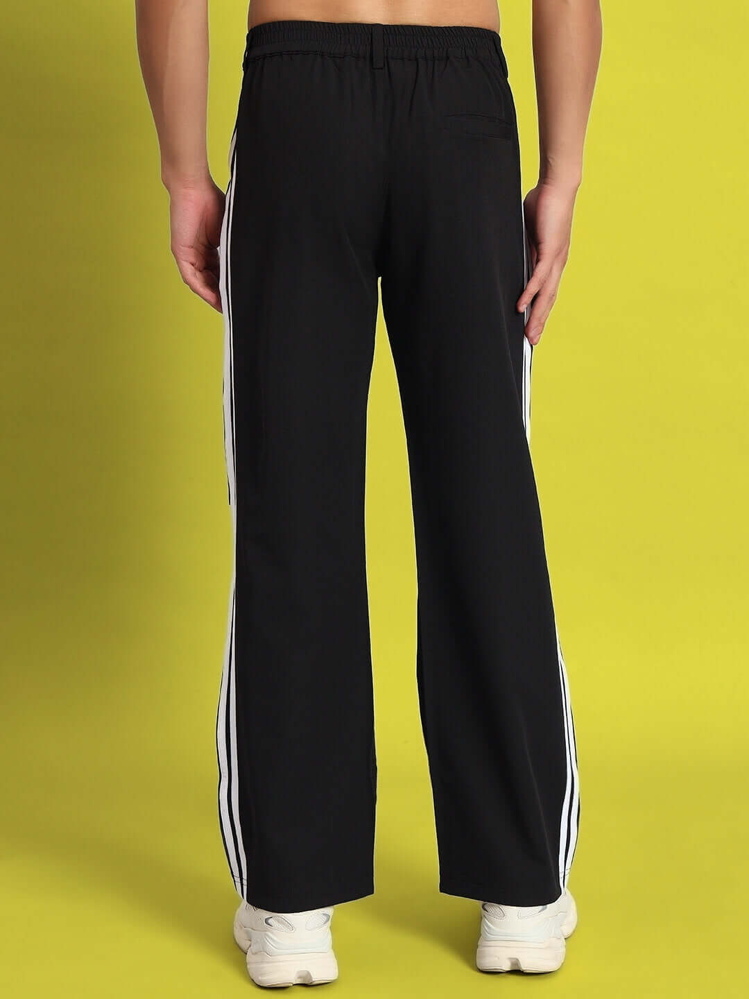 Back view of Drove Relaxed Fit Black Cargo Pants with white stripes, customizable for a perfect fit, displayed against a yellow background.