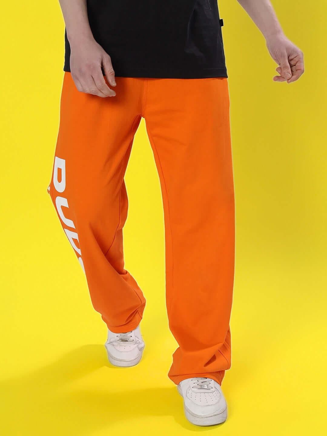 Man wearing DUDS Limited Edition Orange Joggers with white sneakers on a yellow background.