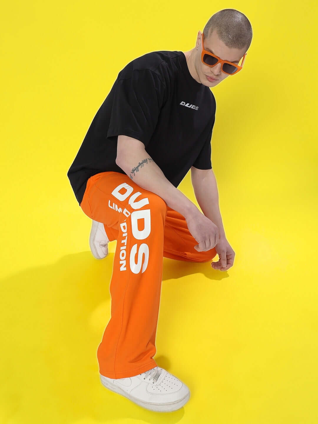 Model wearing DUDS Limited Edition Orange Jogger with bold logo on yellow background, showcasing unique streetwear fashion.