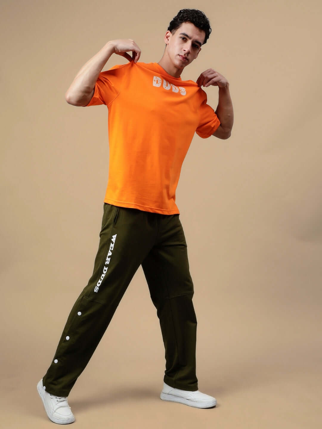 Man modeling DUDS Racer Joggers in olive green with orange DUDS t-shirt, showcasing casual style and comfort.