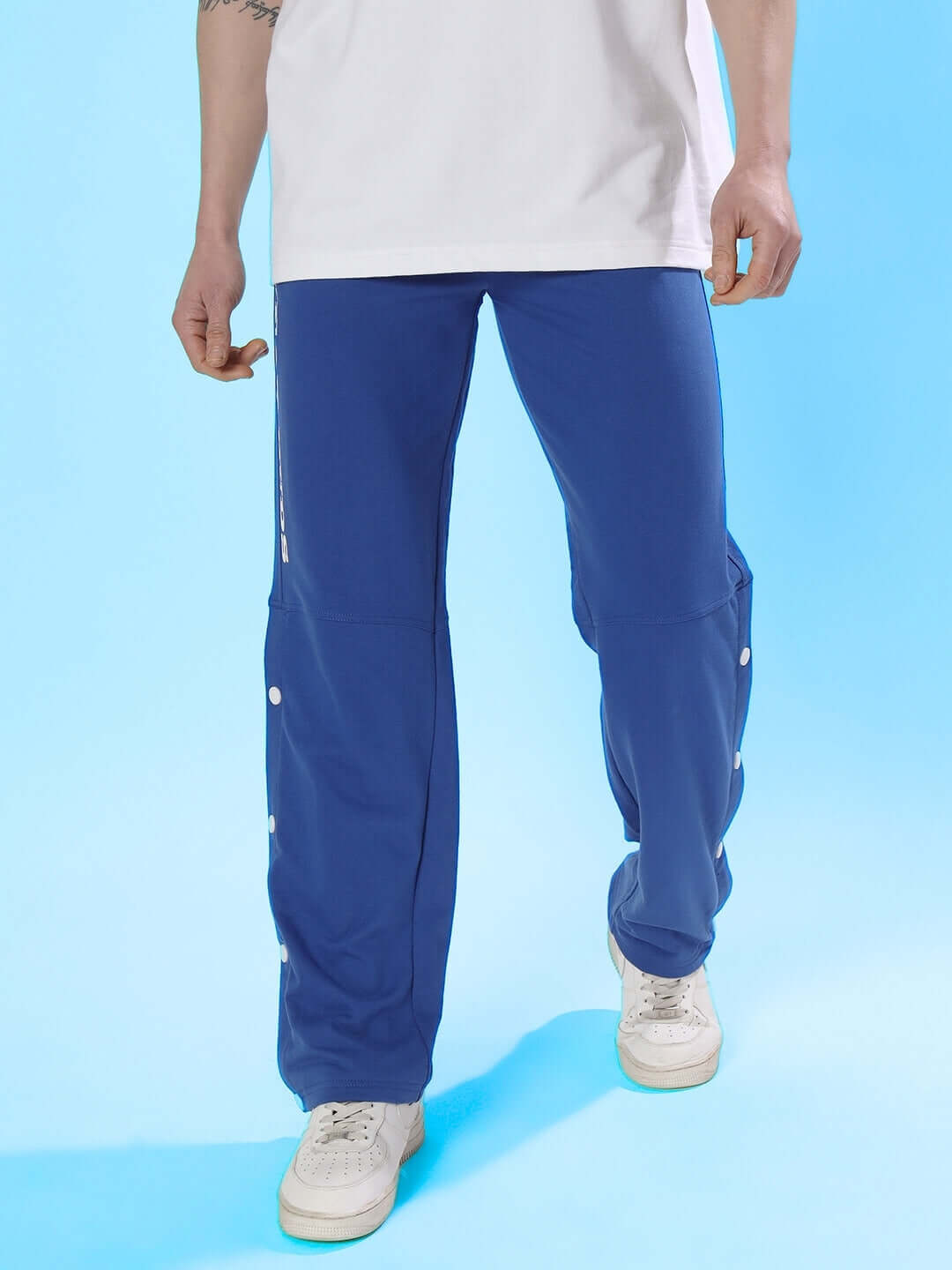 Man wearing DUDS RACER joggers in royal blue with casual white sneakers against a blue background.