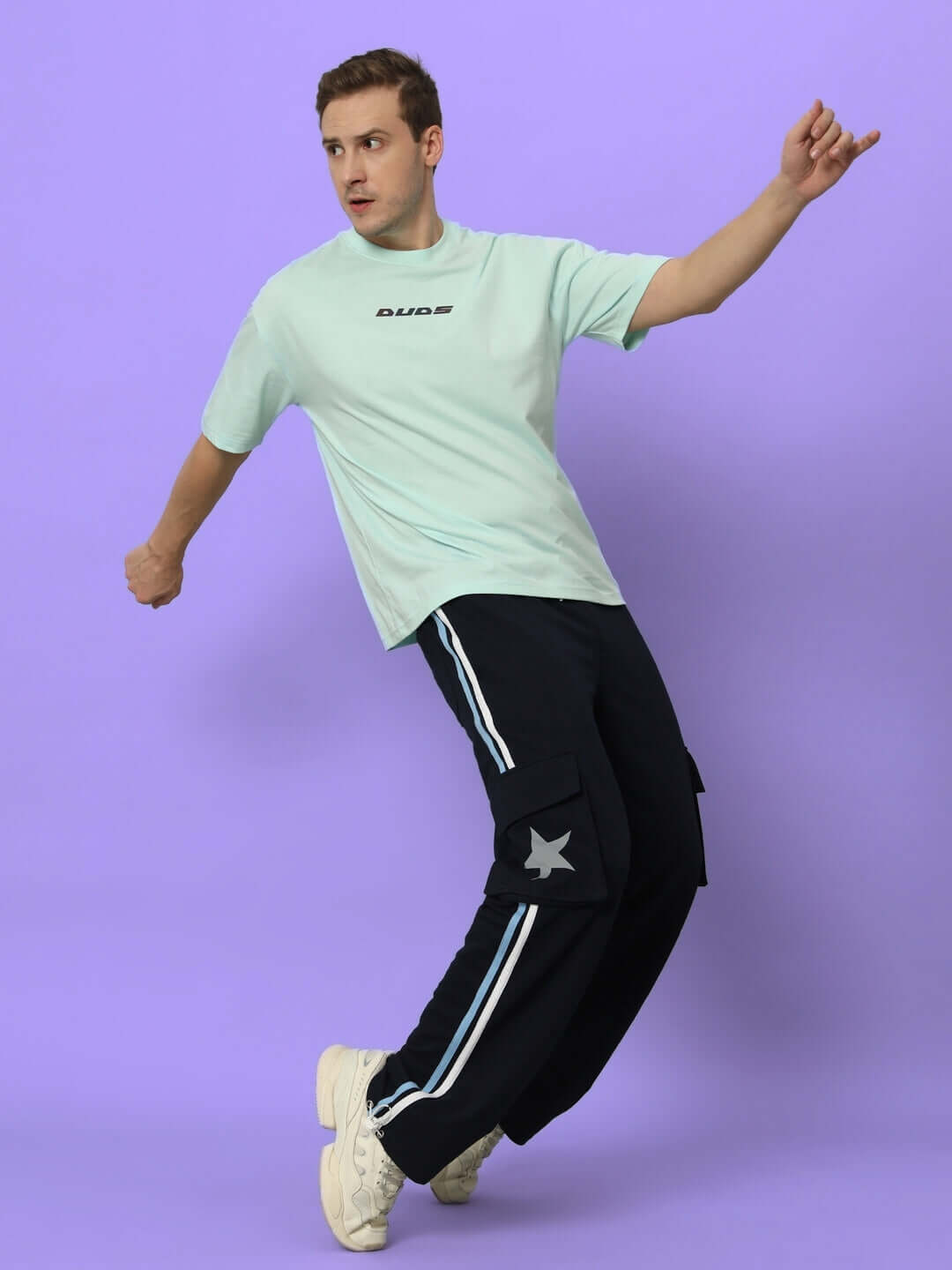 Model wearing DUDS Force Joggers in navy blue, featuring stylish cargo pockets, against a purple background, showcasing modern casual fashion.