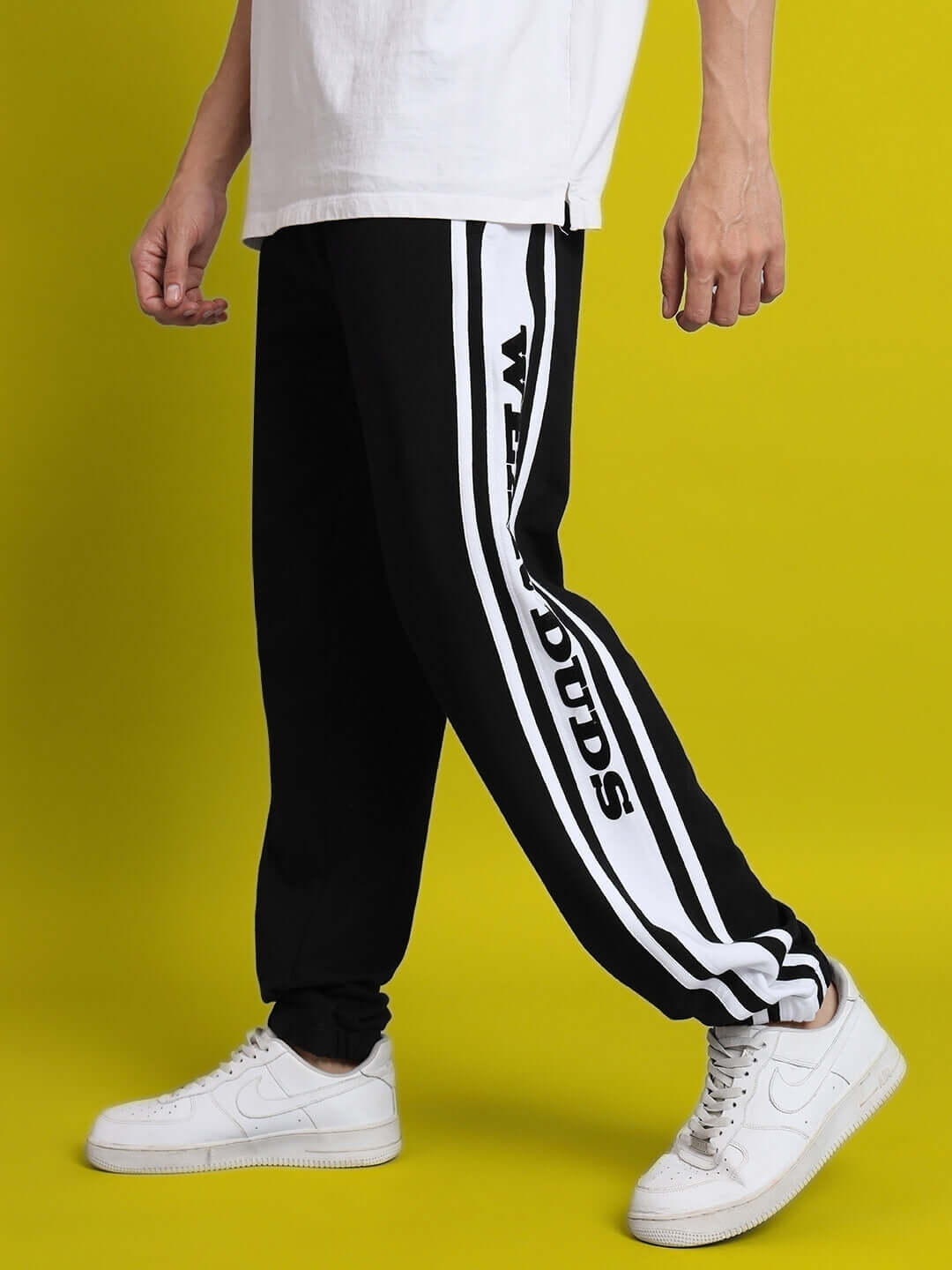 Person wearing DUDS HD contrast panel joggers in black and white with custom fit option, showcasing side profile against a yellow background.