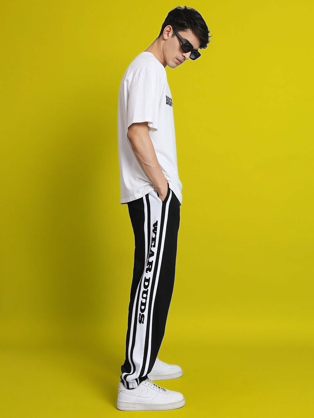Model wearing DUDS HD Contrast Panel Joggers in black and white, featuring bold side lettering, posed against a bright yellow background.