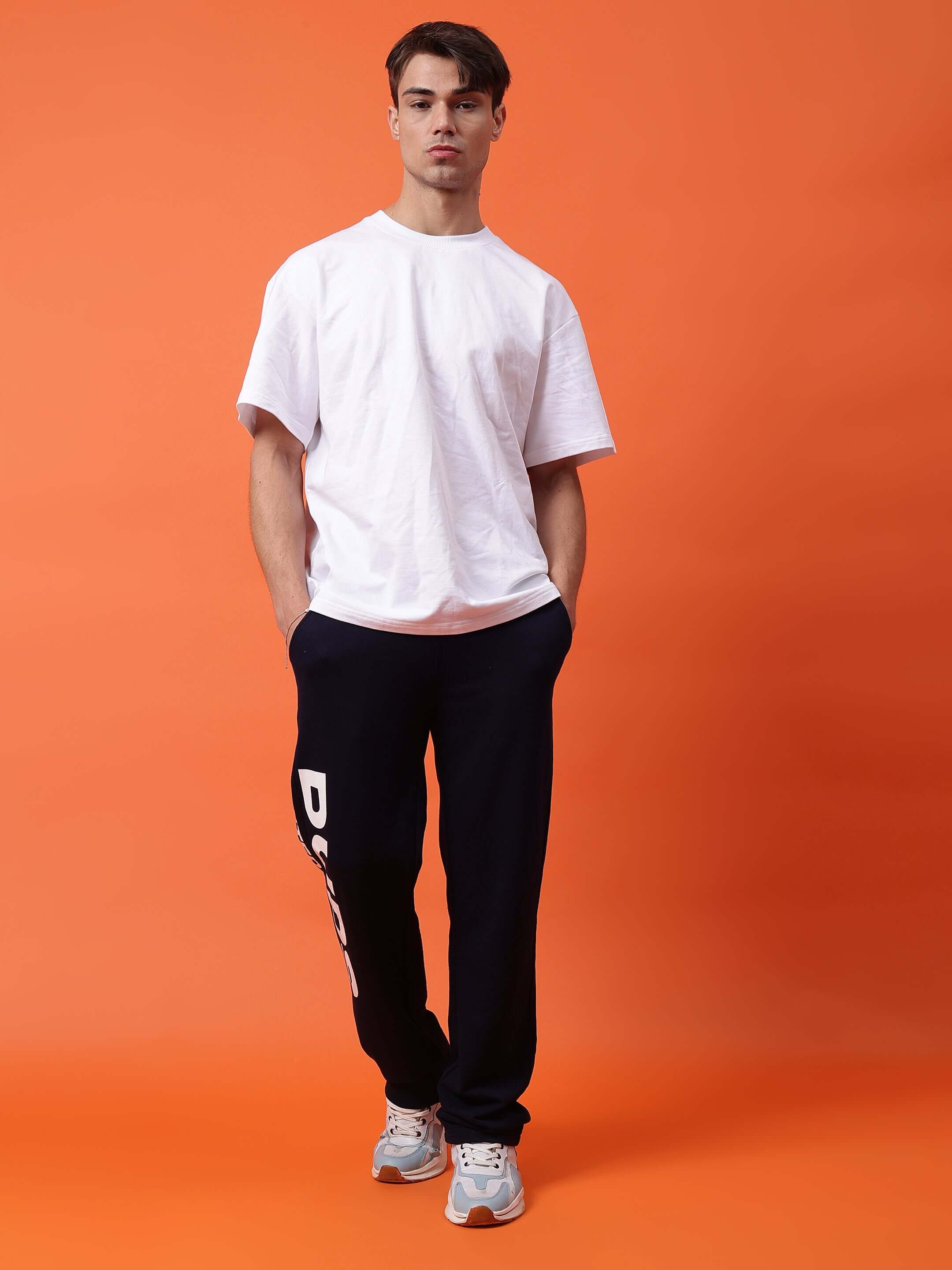 Male model wearing DUDS Limited Edition Navy Blue Jogger with white t-shirt against orange background.