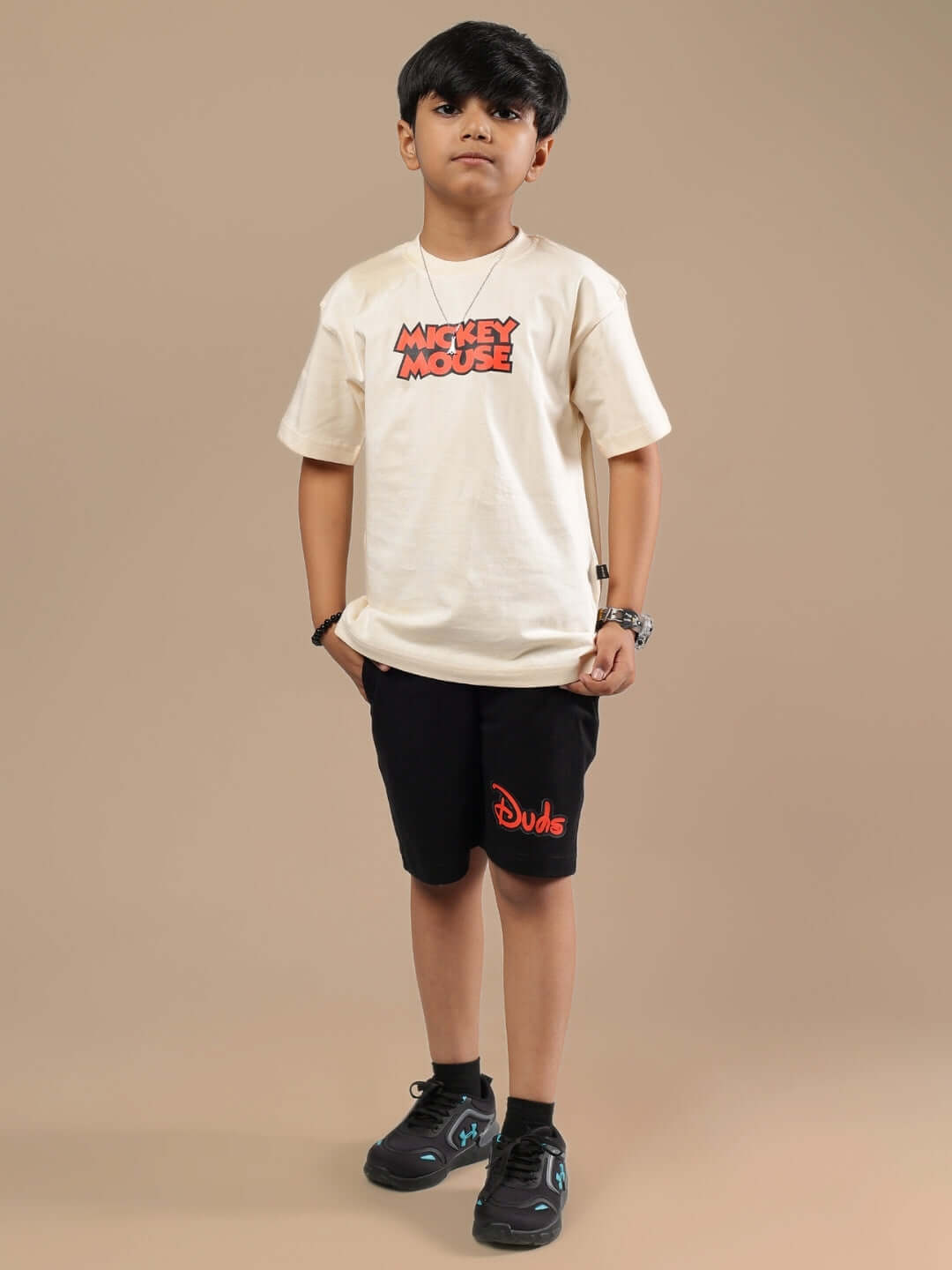 Boy wearing DUDS MOUSE CO-ORD FOR BOYS & GIRLS BEIGE-BLACK outfit, featuring beige top and black shorts, standing against a beige background.