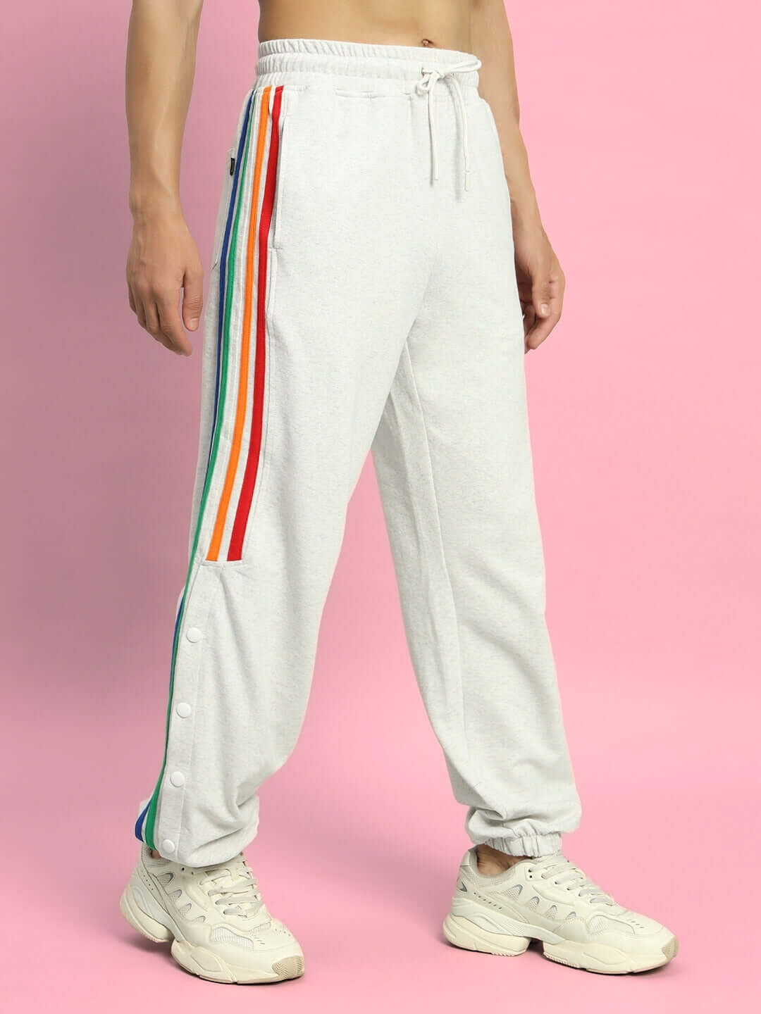 Model wearing DUDS Prism Colorful Stripe Joggers in melange grey with rainbow stripes, standing on a pink background.
