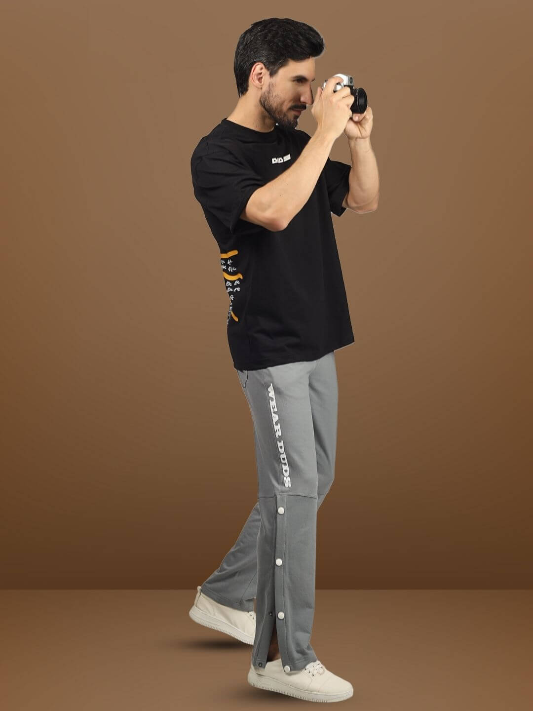 Person wearing grey DUDS RACER JOGGERS captures a moment with a camera, showcasing casual style and custom fit options.