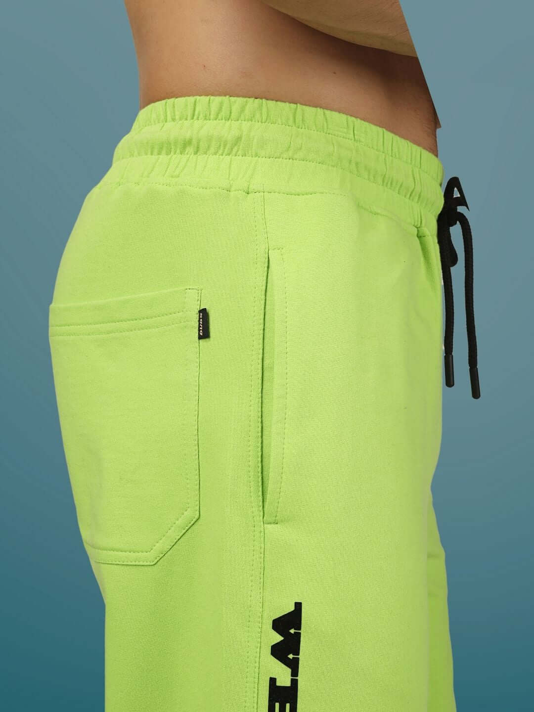 Close-up of neon green DUDS RACER joggers showing elastic waistband and side pocket.
