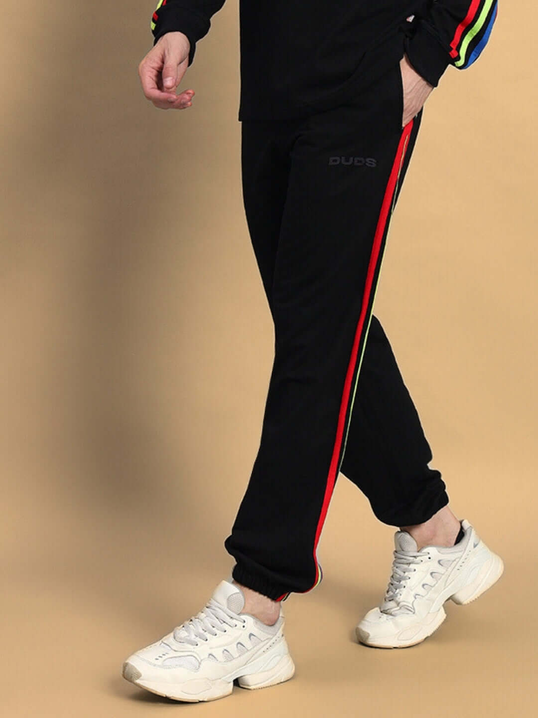 Model wearing DUDS Rainbow Colorful Stripe Joggers in Black with white sneakers, showcasing vibrant side stripes.