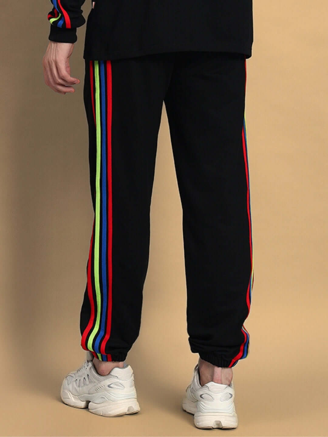 Back view of black joggers with rainbow-colored stripes, worn with white sneakers, showcasing trendy and vibrant design by DUDS.