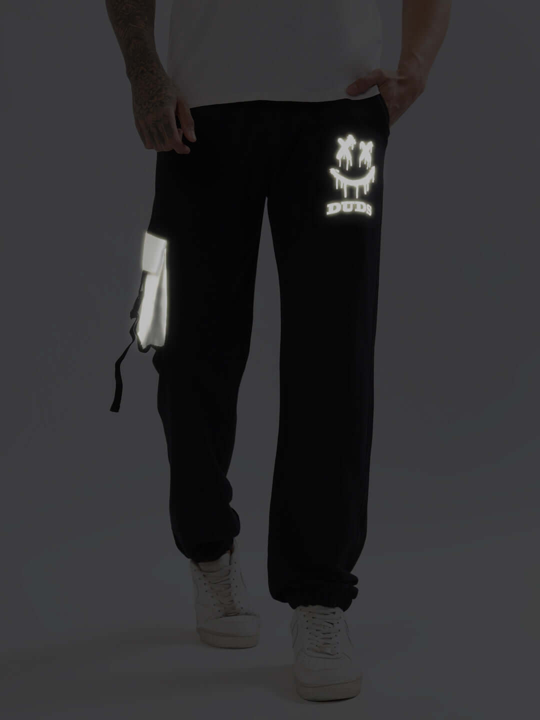 Model wearing DUDS Smiley Reflector Cargo Jogger in black, featuring reflective designs and adjustable fit.