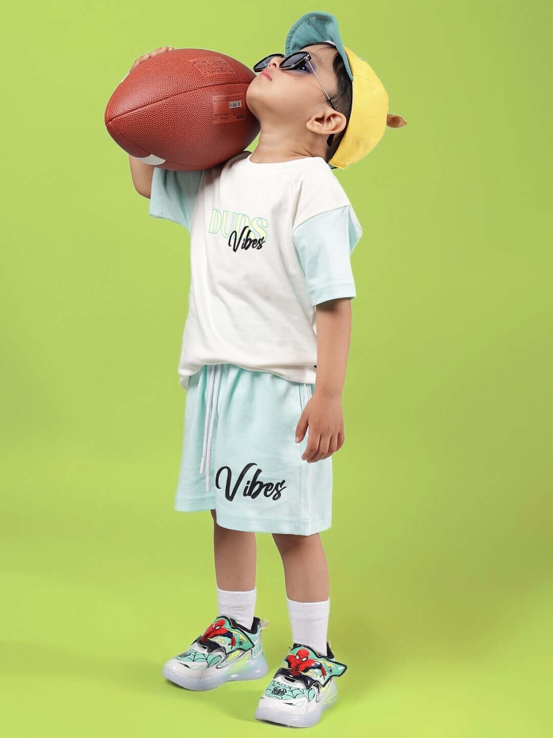 Child wearing DUDS VIBES CO-ORD FOR BOYS & GIRLS OFF WHITE-BLUE playing with a football on a lime green background.