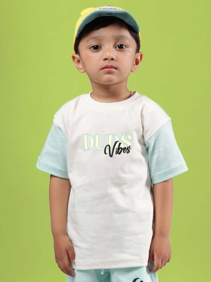Child wearing DUDS VIBES T-SHIRT FOR BOYS GIRLS OFF WHITE-BLUE standing against green background