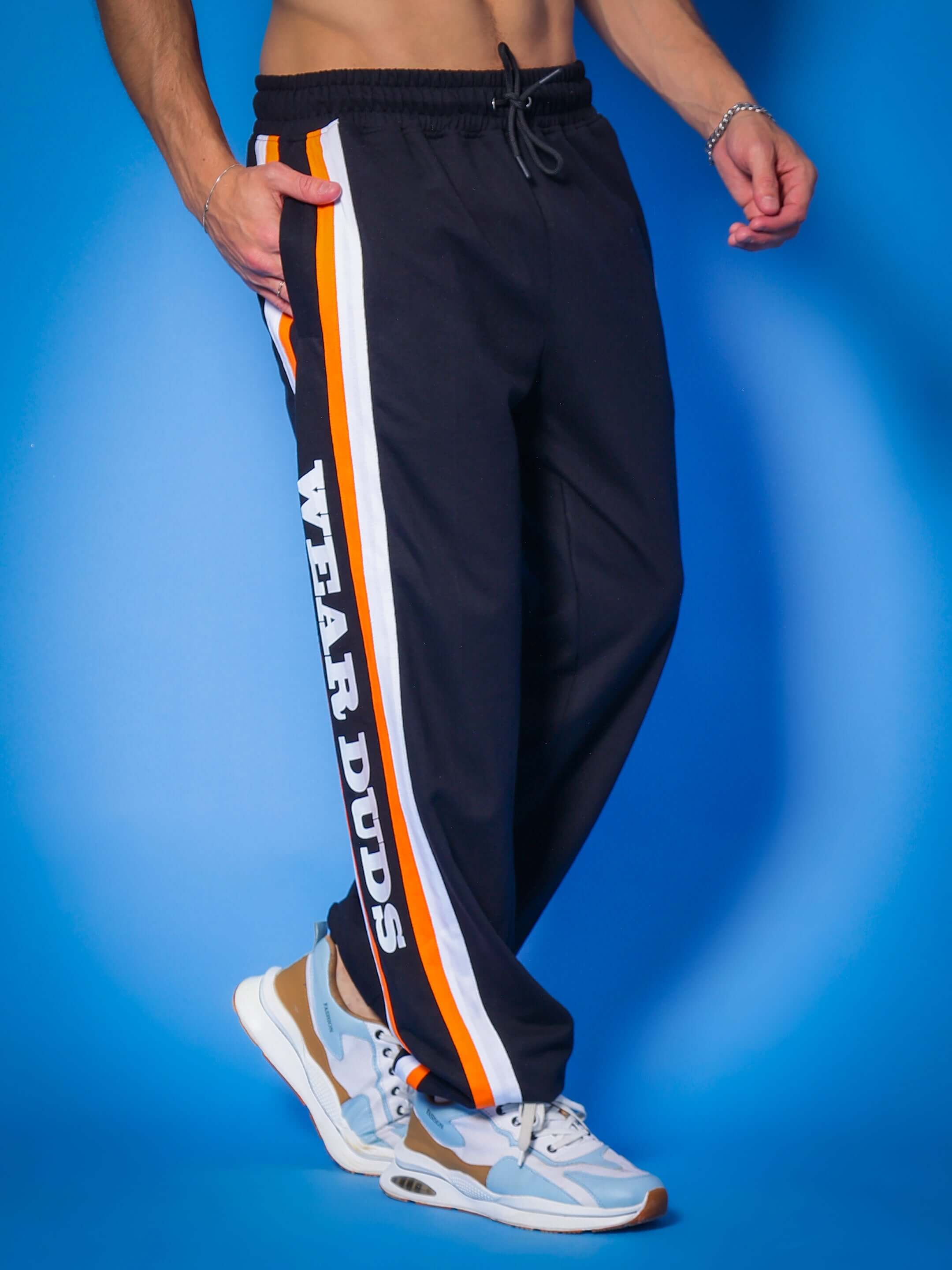 Man wearing DUDS HD Bolt Joggers in black with stripe detail and 'Wear DUDS' text, standing against a blue background.