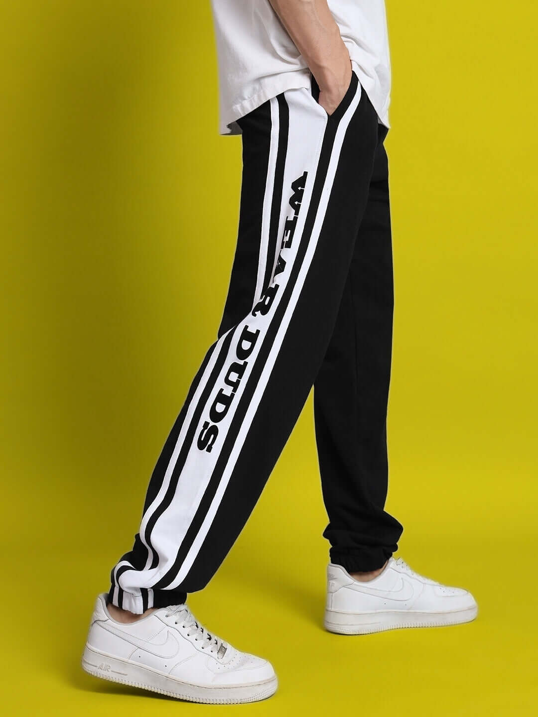 Contrasting black and white joggers with "Wear Duds" lettering, worn with white sneakers against a vibrant yellow background.