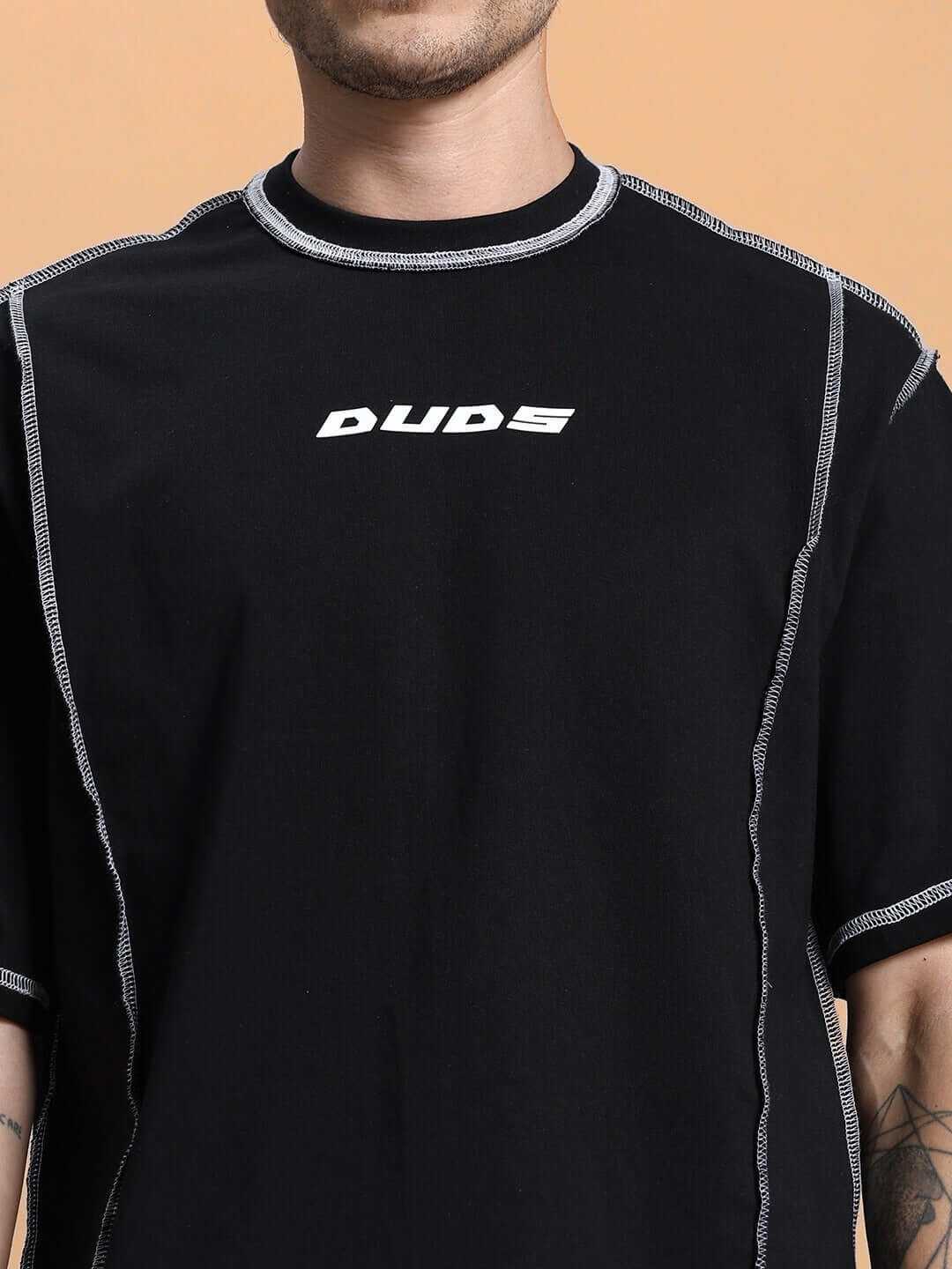 Close-up of a person wearing a DYNAMIC OVER-SIZED CLASSIC T-SHIRT BLACK with white stitching and brand logo.