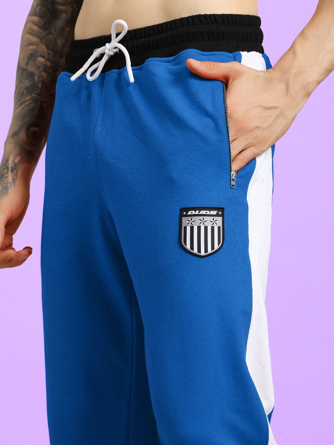 ELEGANT RELAXED-FIT JOGGERS BLUE with side pocket detail and drawstring waistband, modeled against a purple background.