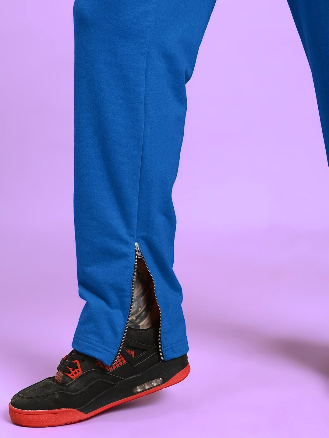 Close-up of ELEGANT RELAXED-FIT JOGGERS BLUE showing ankle zipper with sneaker on purple background.
