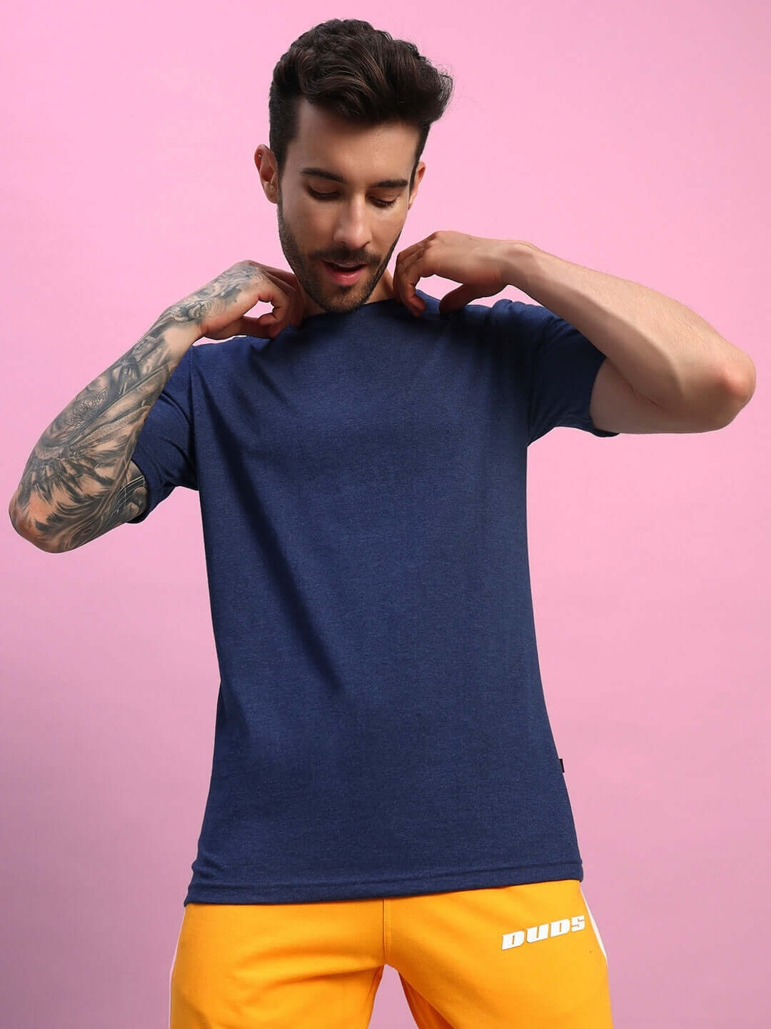 Man wearing ELEX REGULAR FIT T-SHIRT NAVY BLUE with yellow shorts against pink background.