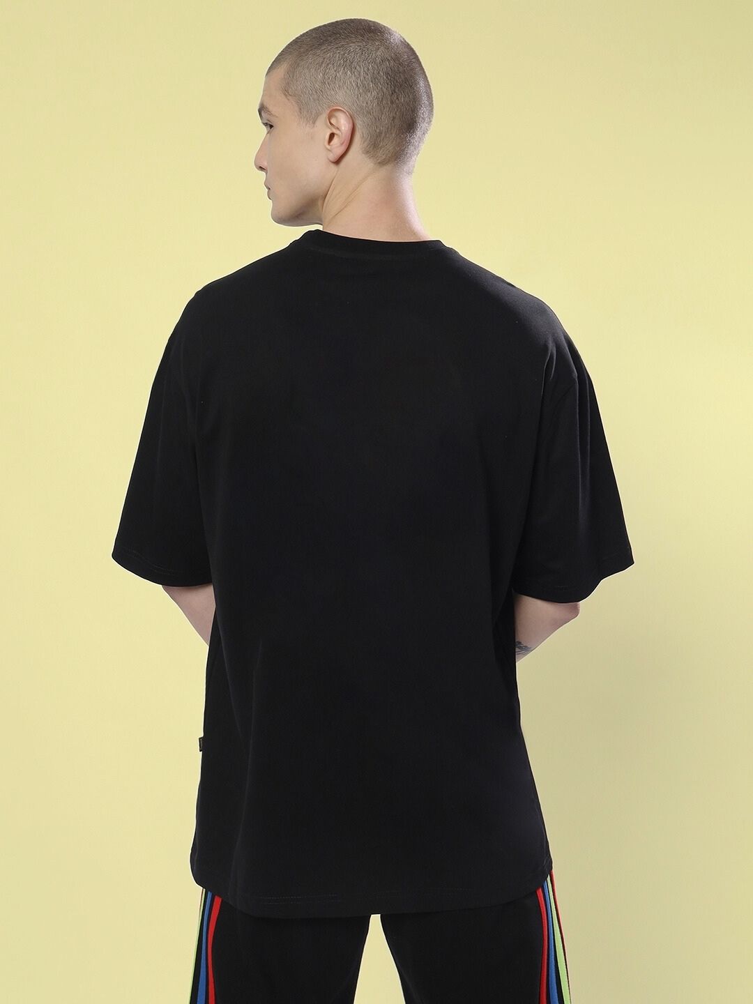 Model wearing END THE MADNESS OVER-SIZED T-SHIRT BLACK with back view on yellow background.