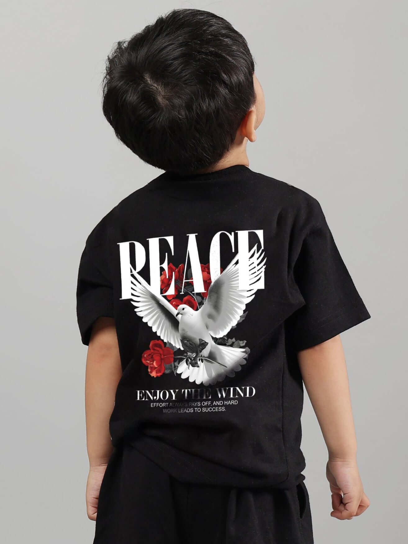 Child wearing a black 'Enjoy the Wind' t-shirt with dove and rose design, suitable for boys and girls.