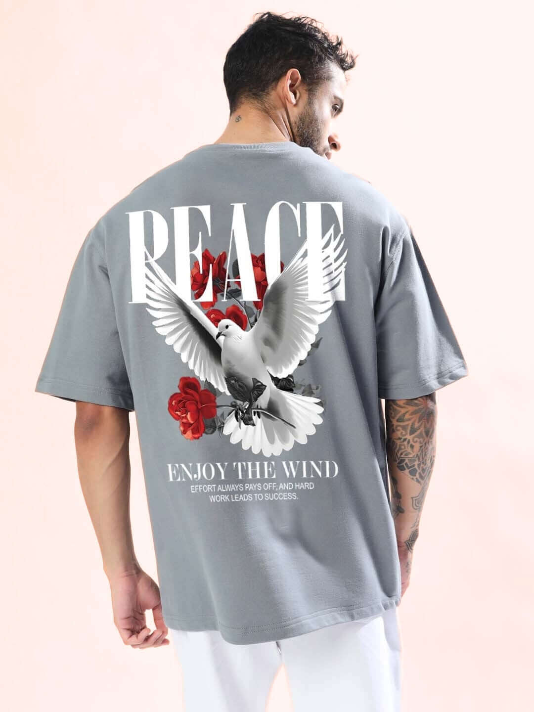Man wearing 'Enjoy The Wind' oversized grey T-shirt with dove and rose design on the back, promoting peace and comfort.