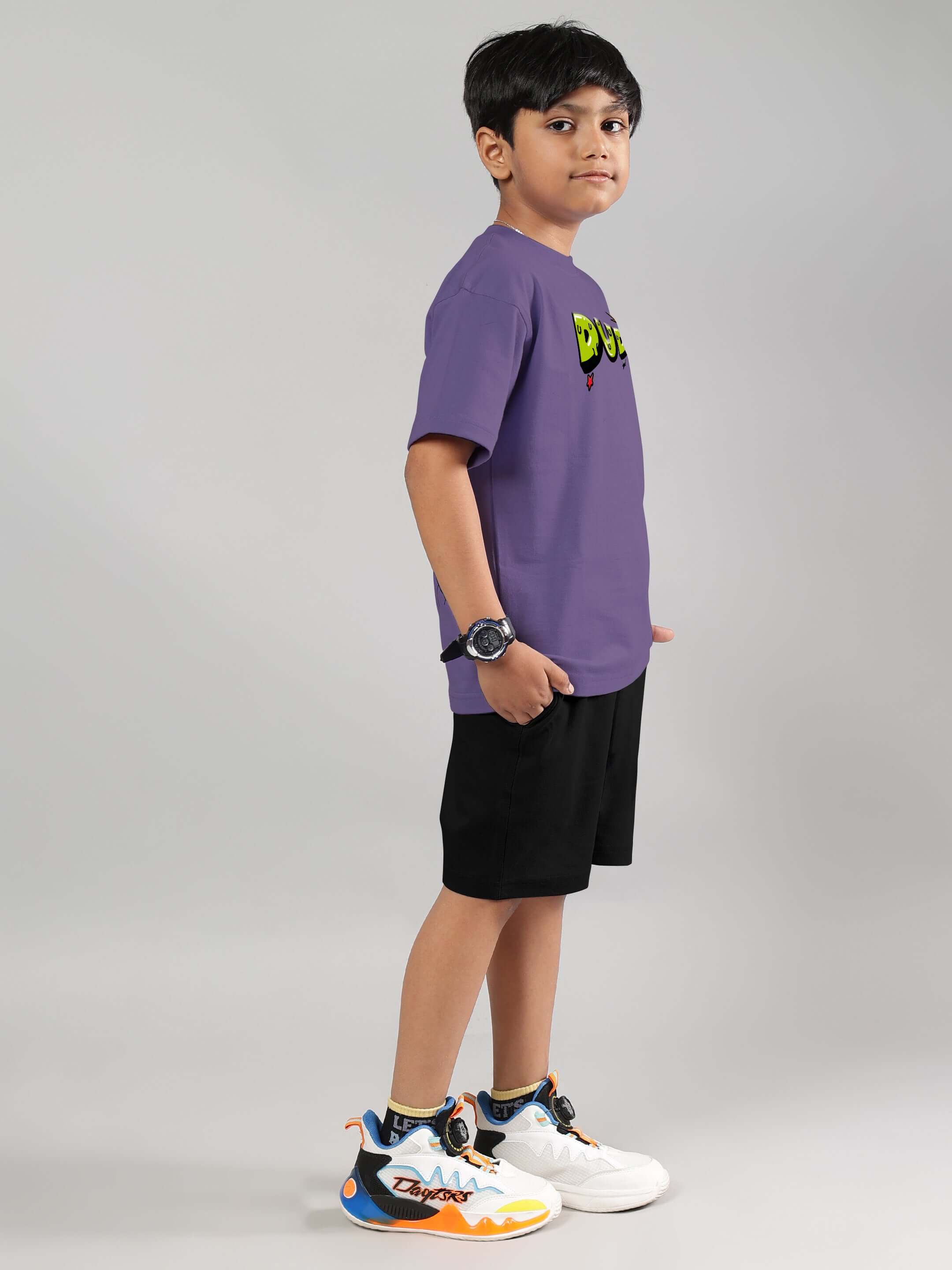 Boy wearing ESCAPED TWEETY CO-ORD FOR BOYS GIRLS WISTERIA PURPLE BLACK, featuring purple top and black shorts, standing in profile.
