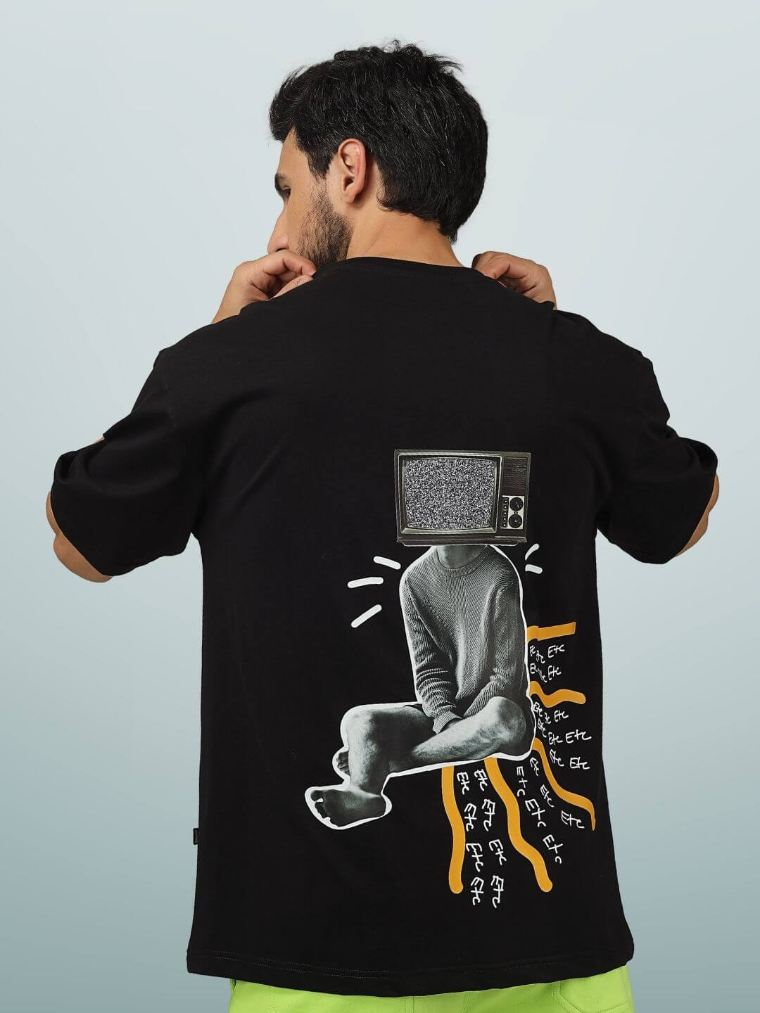 Man wearing an ETCETERA oversized black T-shirt with unique graphic design on the back, customizable size option available.