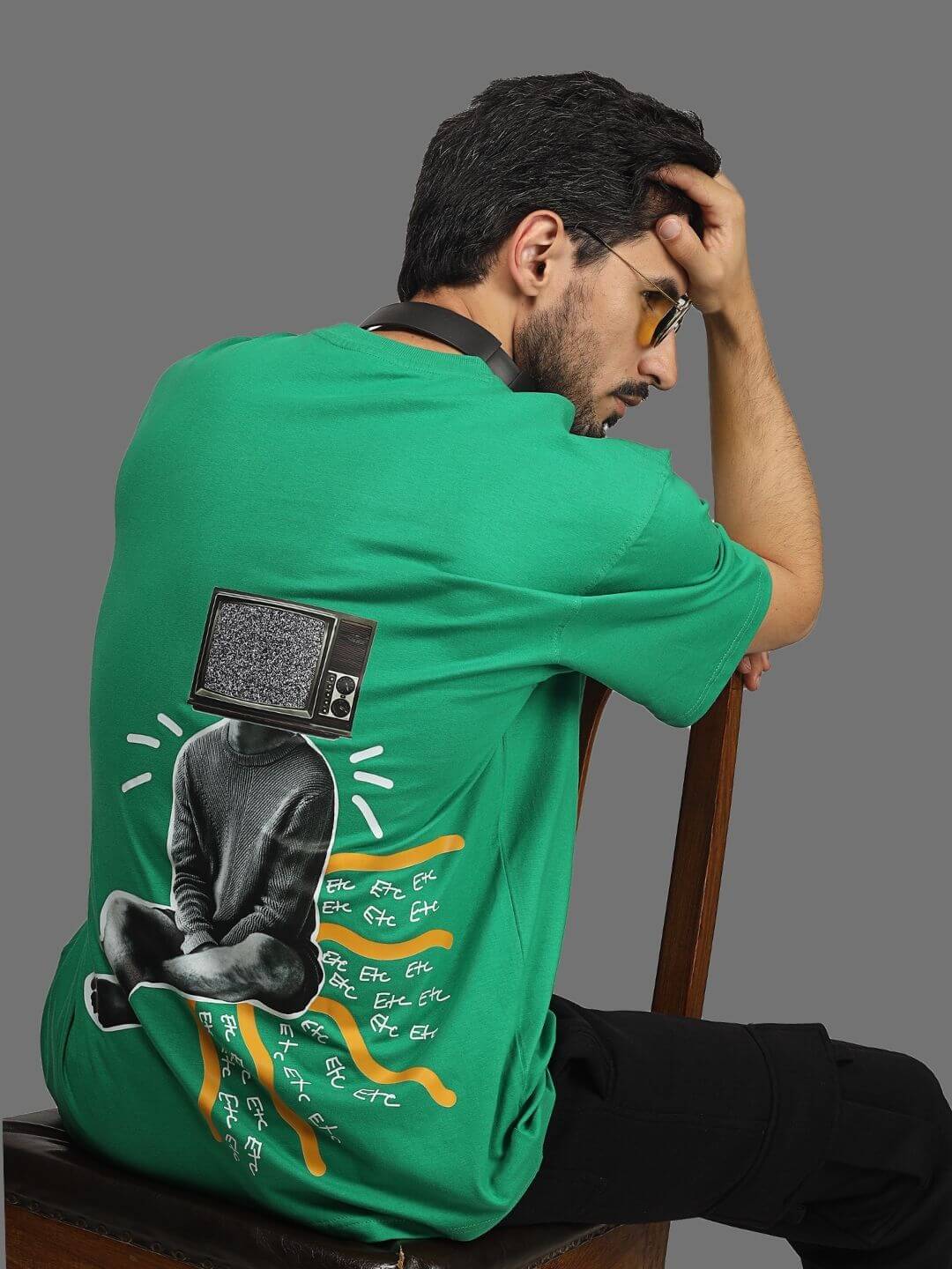 Green oversized t-shirt with unique graphic design, worn by a model sitting on a stool.