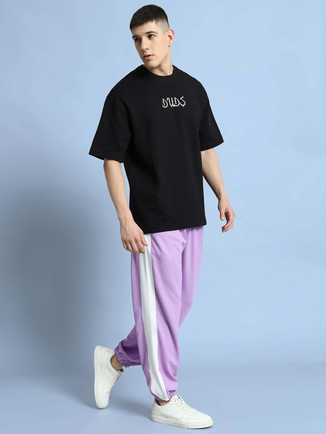 Model wearing EUPHORIA joggers in lavender-white from DUDS, paired with a black t-shirt and white sneakers.