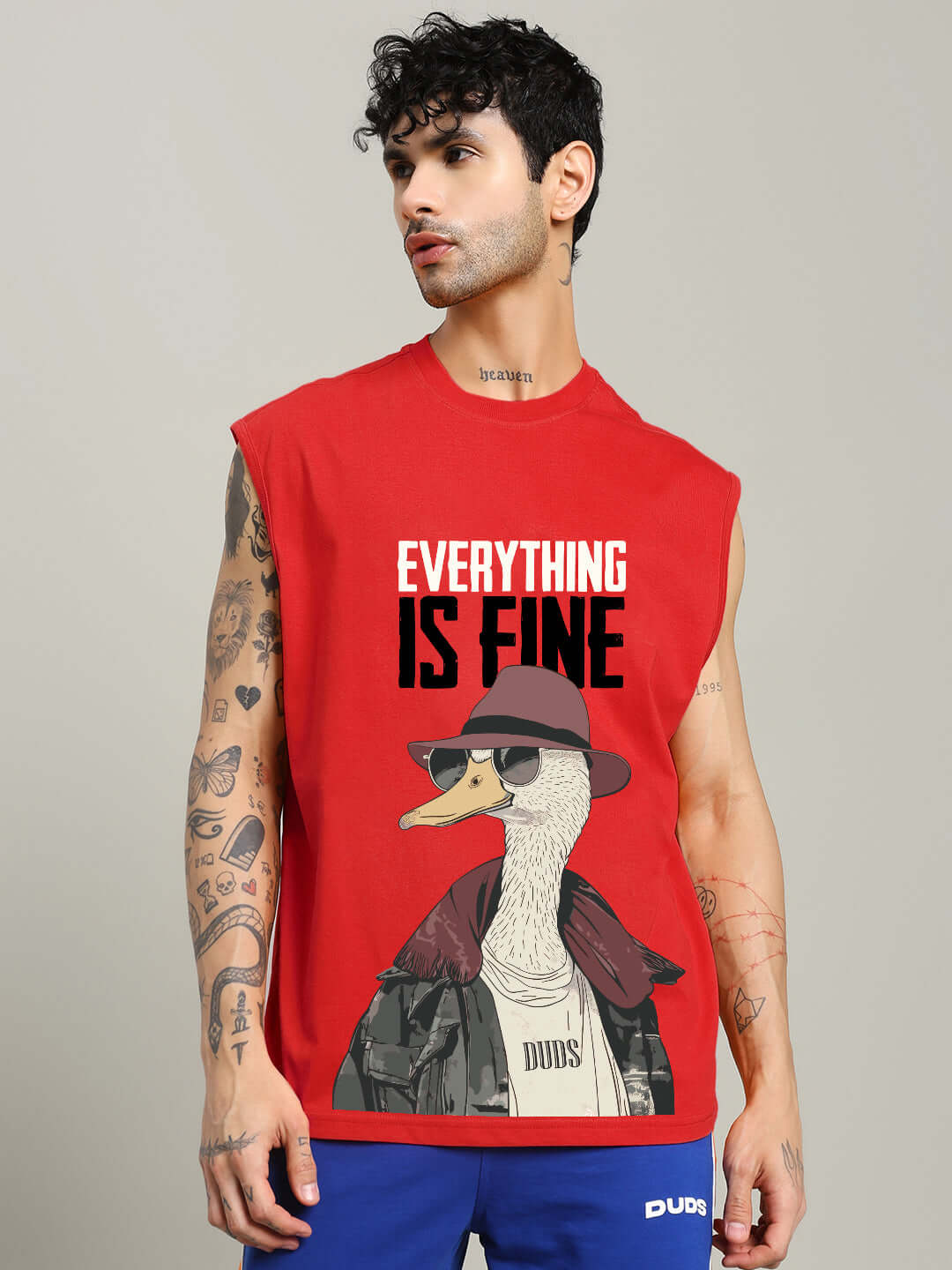 Model wearing red "EVERYTHING IS FINE" gym T-shirt by DUDS featuring a cartoon duck with sunglasses and hat, promoting custom fit option.