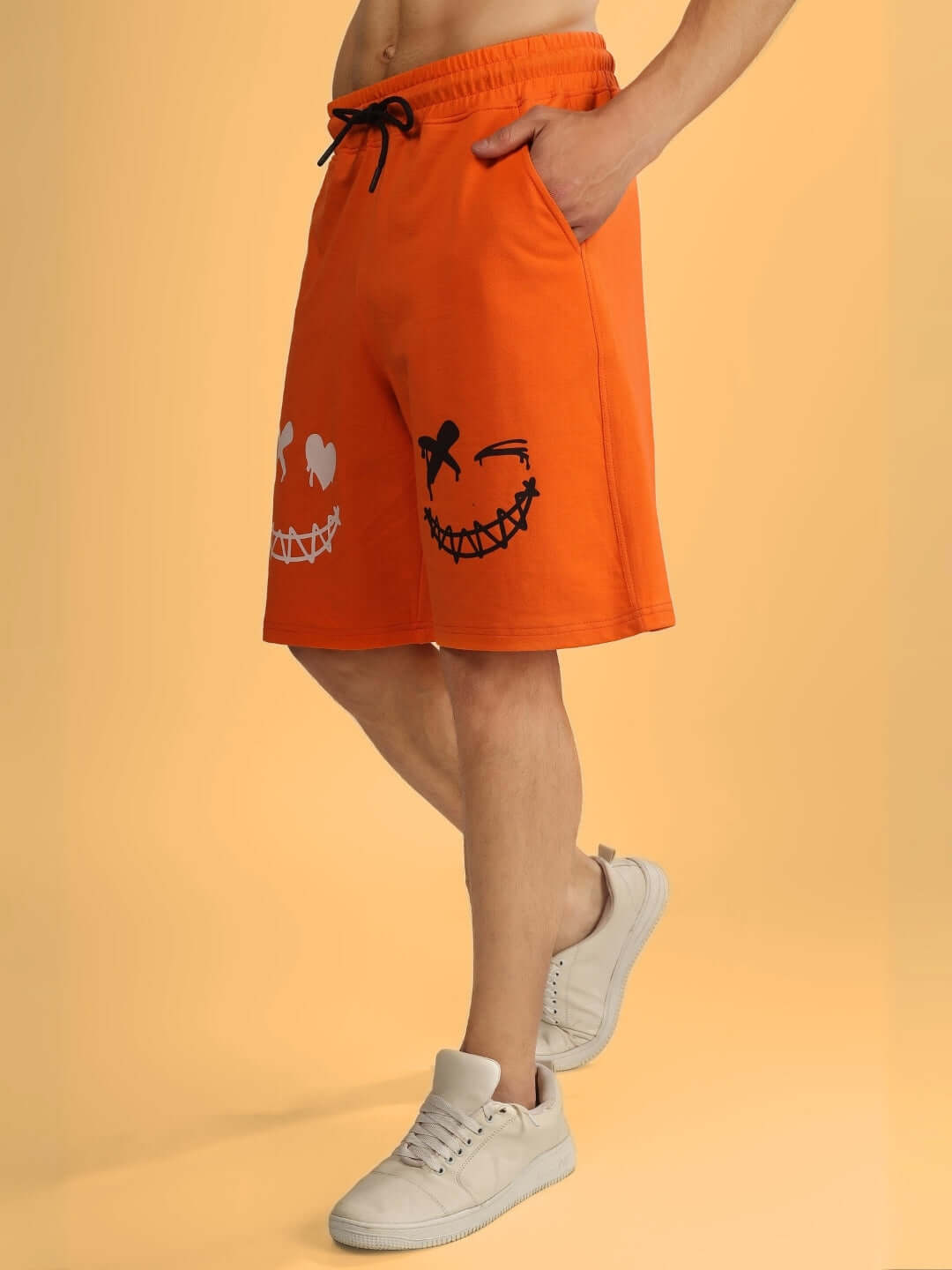 Model wearing orange regular fit shorts with evil smile graphic, featuring pockets and drawstring, perfect for casual wear.
