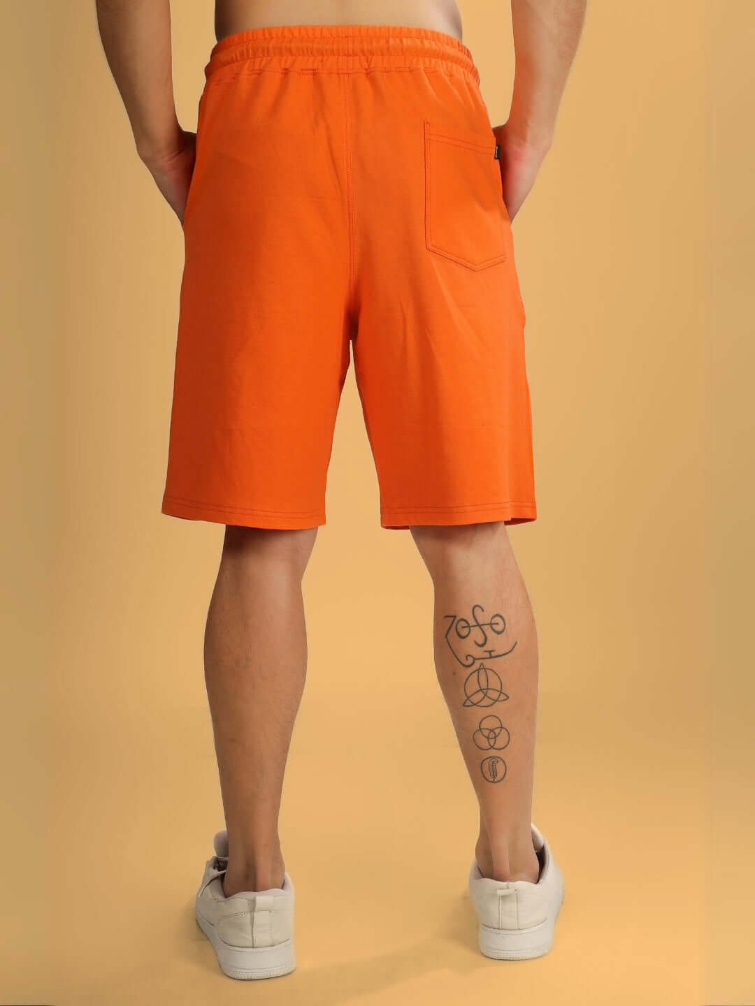 Back view of orange regular fit shorts featuring a pocket, shown on a person with tattooed leg, emphasizing customizable fit options.