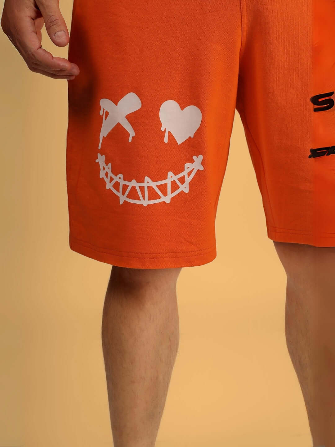 Bright orange shorts with an evil smiley face design featuring crossed eyes and a stitched mouth pattern.