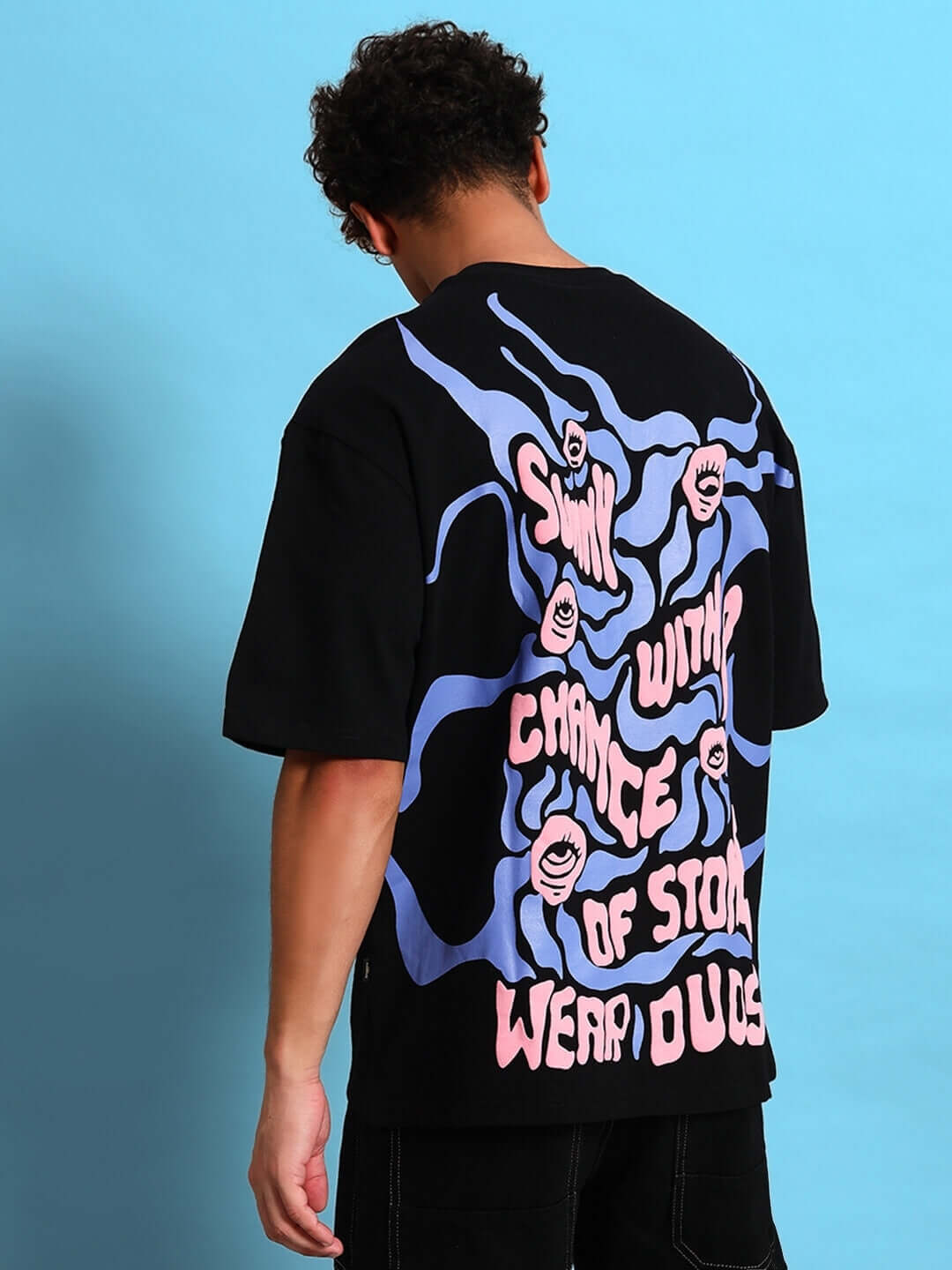 Back view of a model wearing an oversized black T-shirt with eye ball puff print design, showcasing vibrant graphics and text.